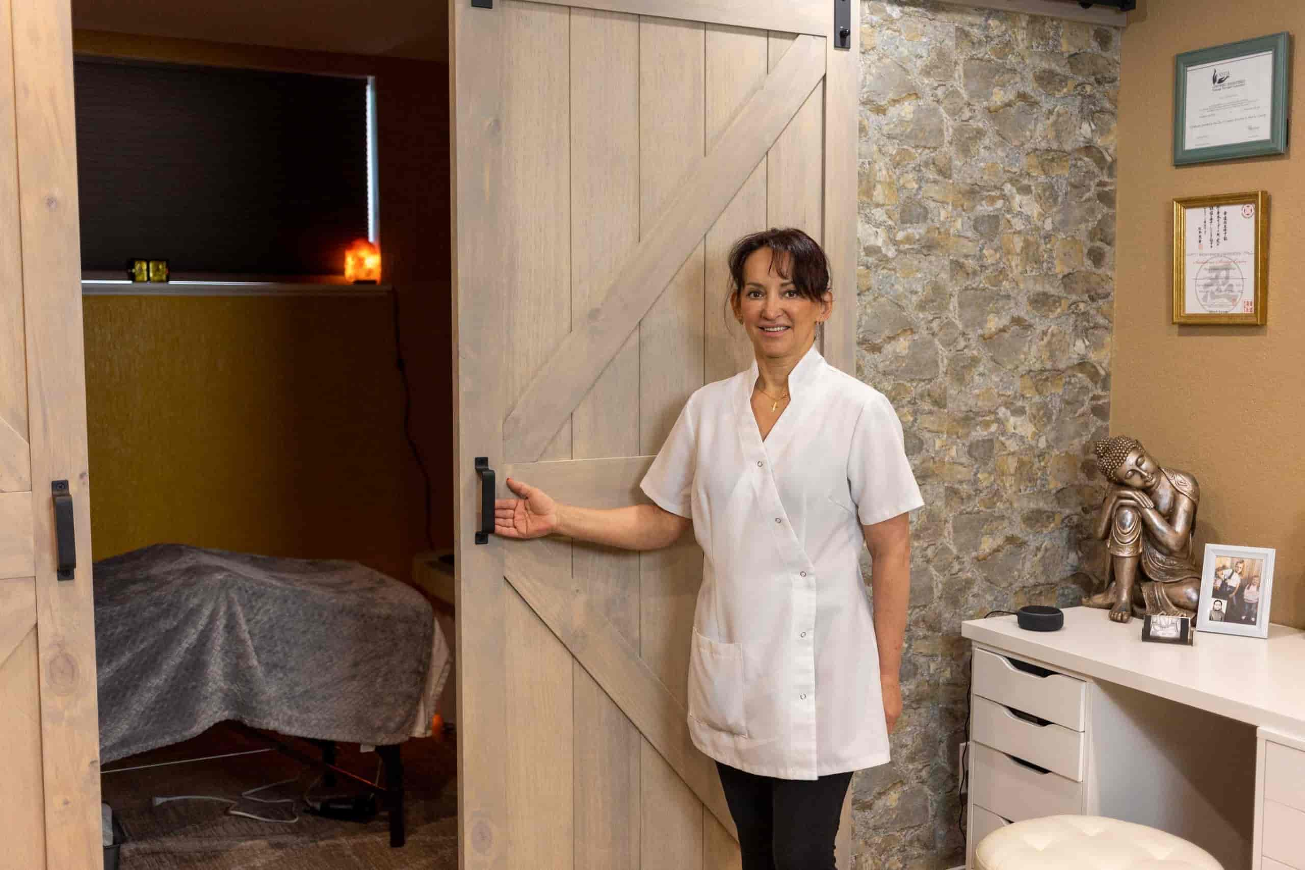 Lena, a licensed massage therapist in Calgary, alberta, stands in front of her barn style door leading to her massage therapy room in the basement of her home in Calgary, Alberta, Canada.