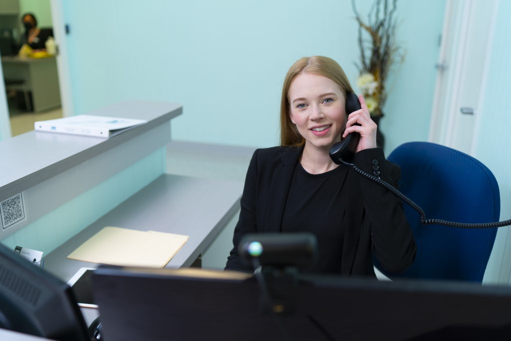 MaKami College business administrative assistant student answering a phone at a desk in an office setting