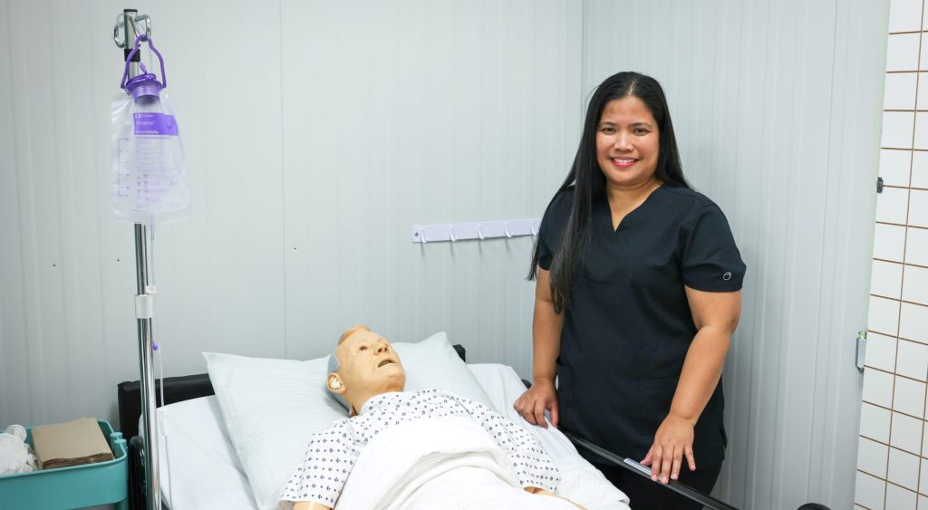 Avelina, a health care aide student in Calgary, Alberta stands next to a dummy patient at class at MaKami College