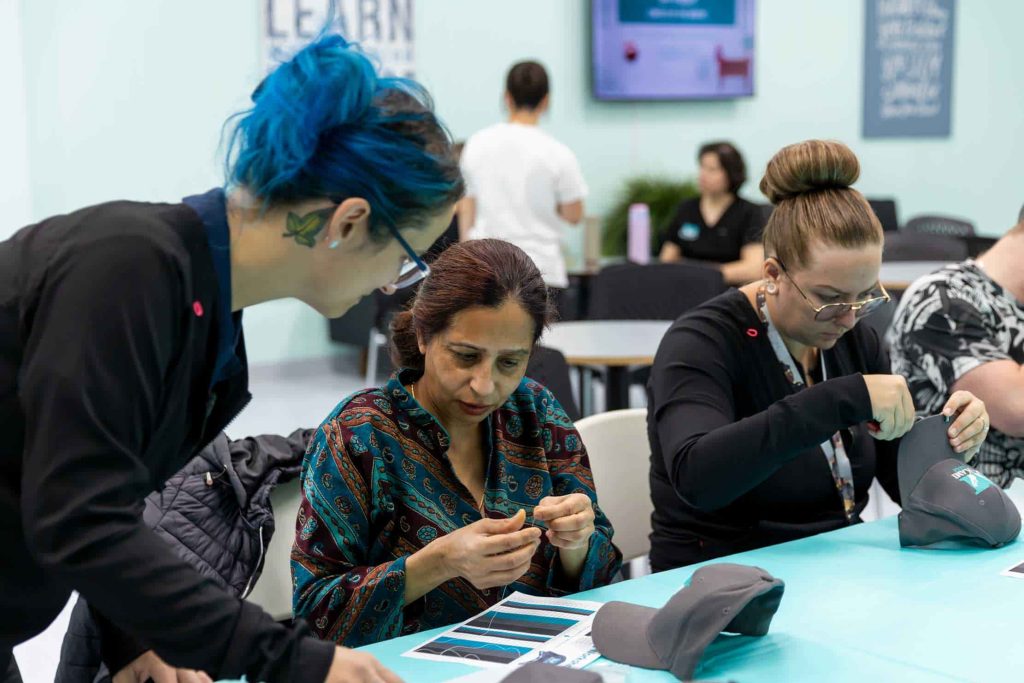 A young Metis teacher with blue hair instructs a student on how to do Metis Indigenous beading in a workshop at MaKami College in Calgary, Alberta, Canada
