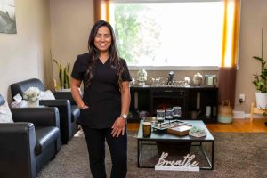 Ilene Reye, a Filipino female with long, dark hair, stands in her massage therapy clinic in Calgary, Alberta, Canada