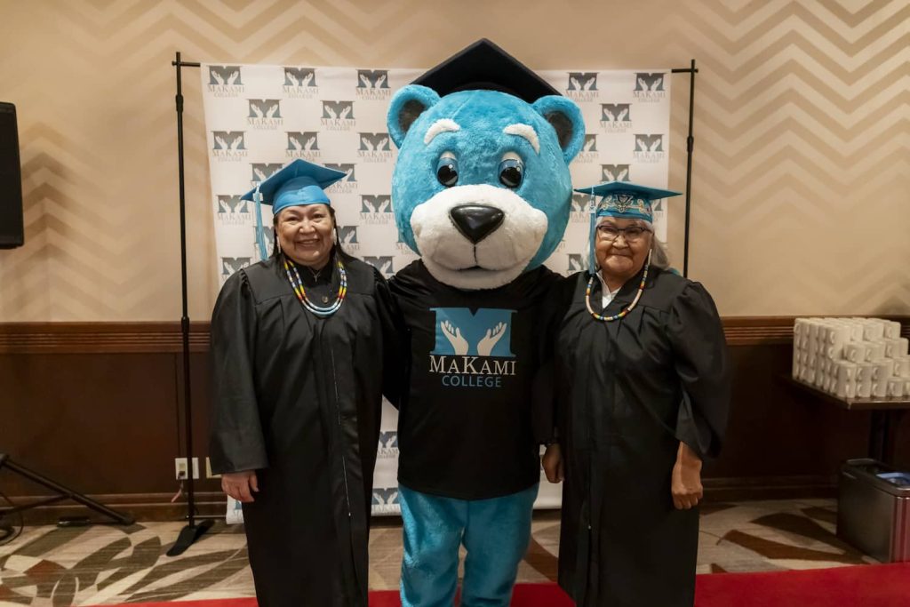 Lisa Smallboy and MaKami Max mascot with her sister Andrea at her graduation from MaKami College's Health Care Aide program