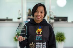 Micah, a young female massage therapy graduate from MaKami College from the Philippines, stands holding a recent award for her massage therapy business in Medicine Hat, Alberta, Canada