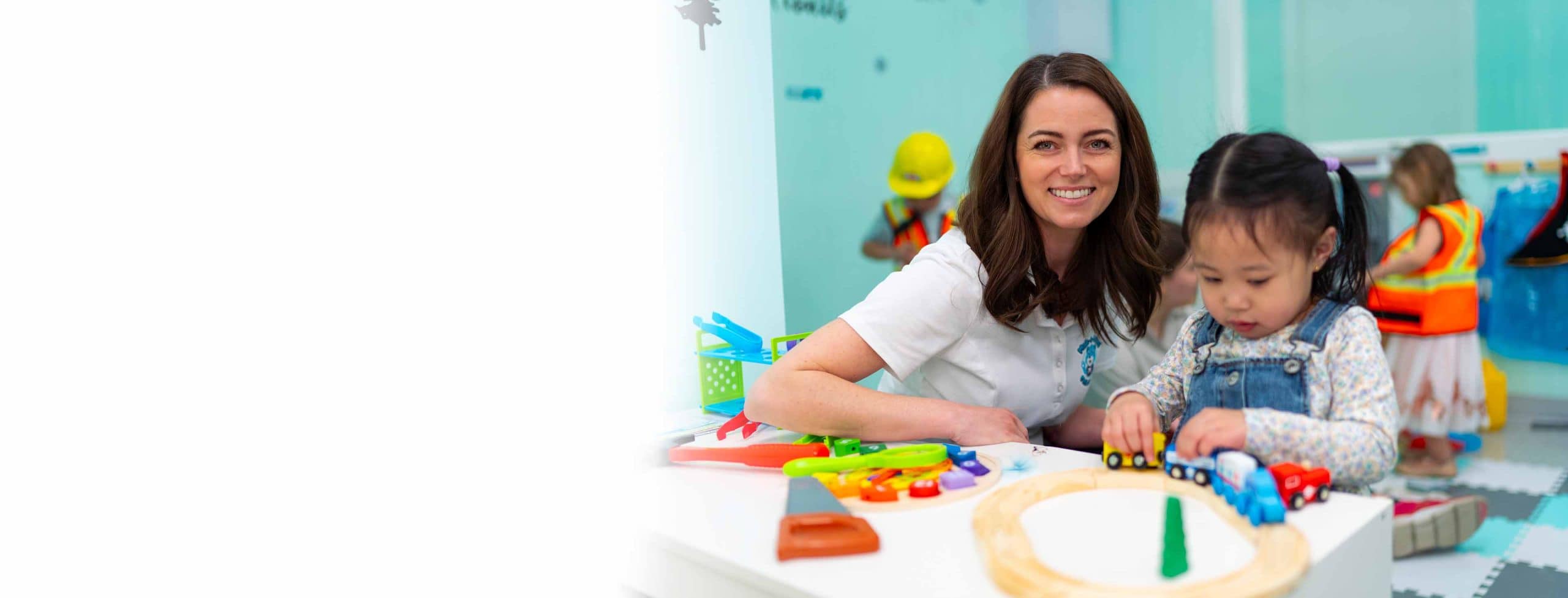 Female MaKami early childhood education (ECE) certificate student with a young child playing with a toy train in a daycare setting