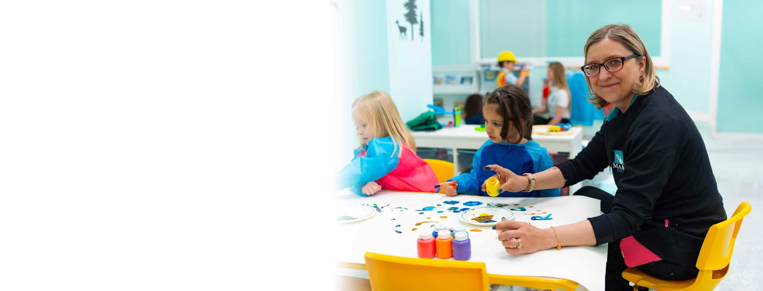 Woman getting hands-on training for her early childhood educator diploma while helping two small children with create art