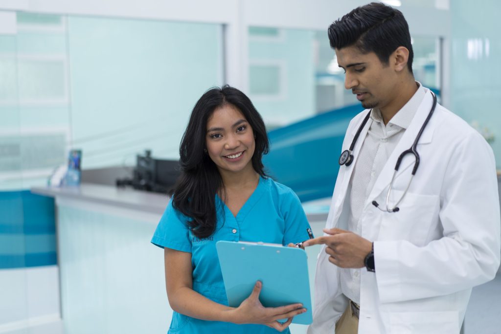 Health Care Aide in blue scrubs collaborating with doctor in Alberta healthcare setting