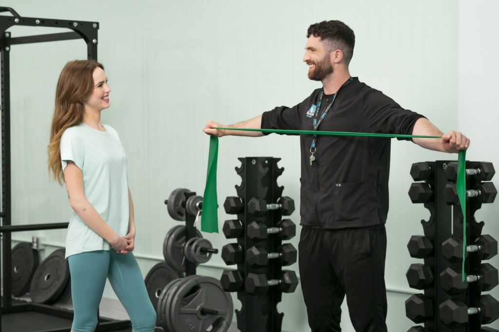 Personal trainer demonstrating green resistance band exercise to female client in gym with weight equipment