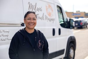 A Filipino female stands in front of her work truck with Milani Warm Touch Massage logo in the background.