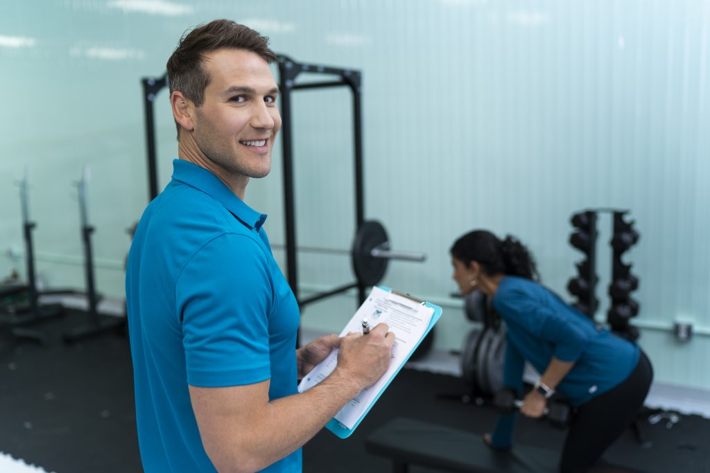 Personal trainer coaching a client in a gym while tracking progress, representing how to become a personal trainer in Canada