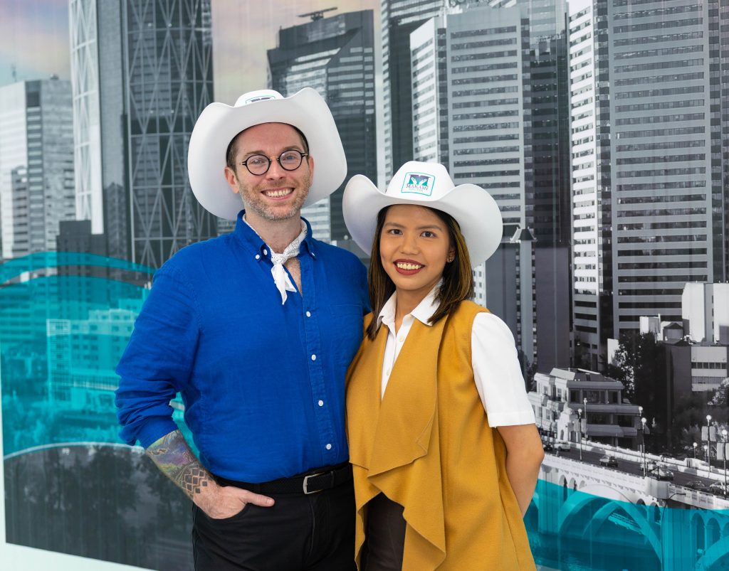 MaKami College team members in branded cowboy hats standing in front of Calgary city skyline office backdrop