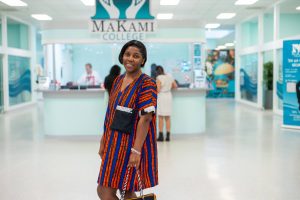 Person standing in the MaKami College campus reception area with the MaKami College logo visible in the background, showcasing a welcoming student environment and education institution in Canada.
